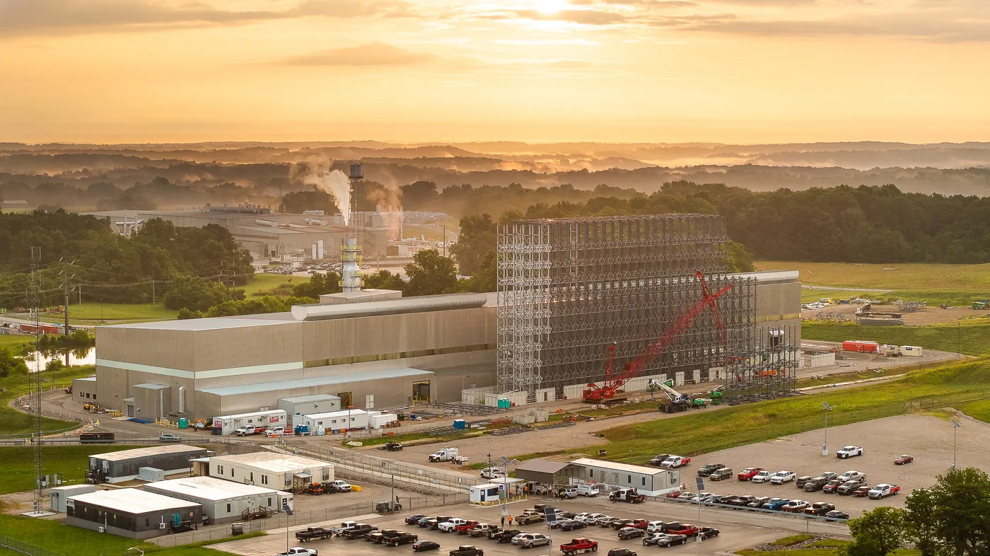 Sunrise aerial of the Russellville automated storage build, a red crawler crane beside a steel scaffold tower above morning fog