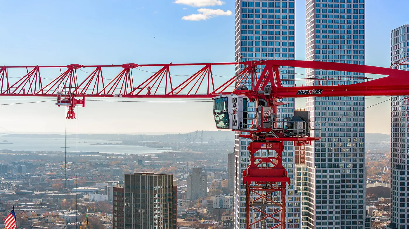 Close aerial of a red tower crane's cab and jib against glass residential towers