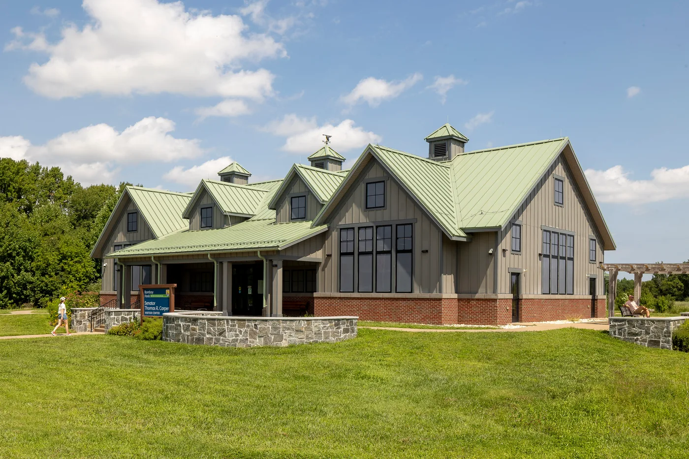 Three quarter view of the visitor center with a walker on the path and a visitor resting on a bench