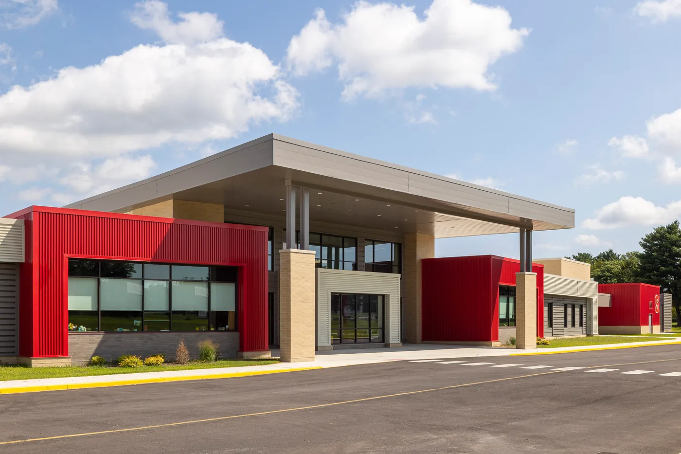 Three quarter view of the school's cantilevered entry canopy between red corrugated volumes