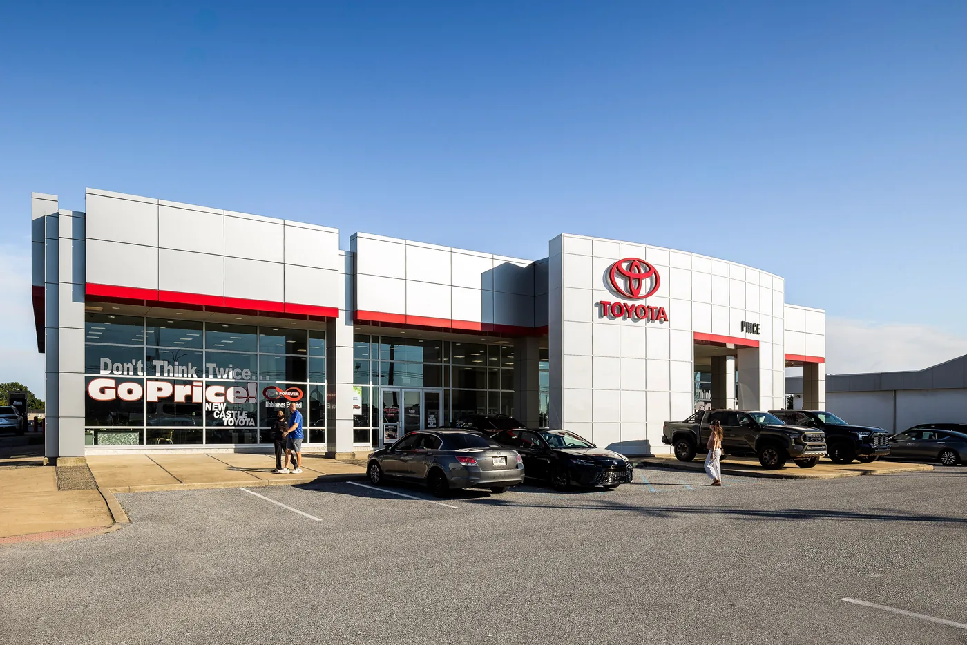Dealership showroom facade with red trim bands, customers outside in late afternoon sun