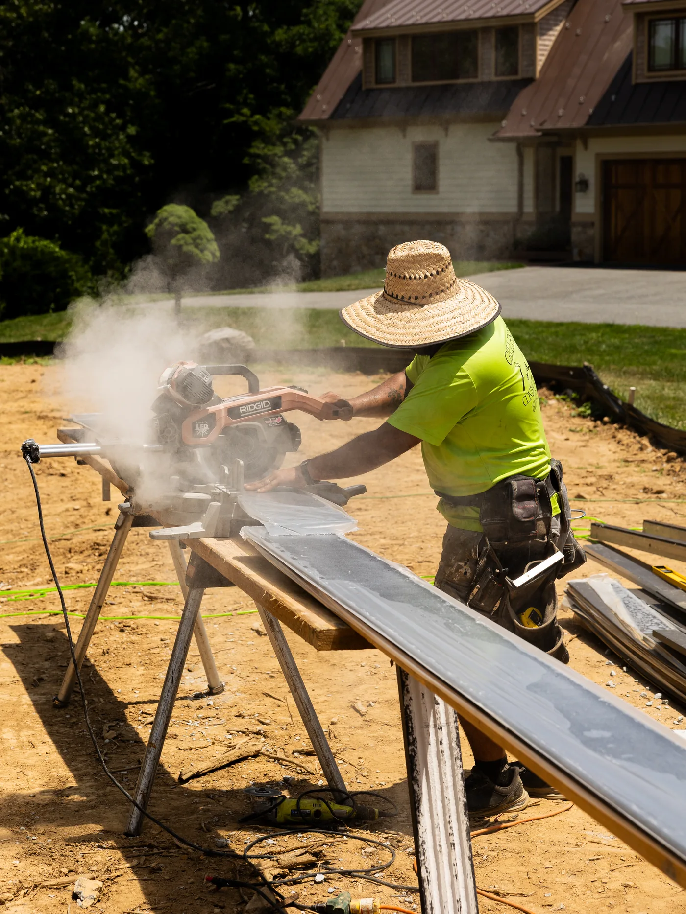 Carpenter in a straw hat cutting siding on a miter saw, sawdust in the air