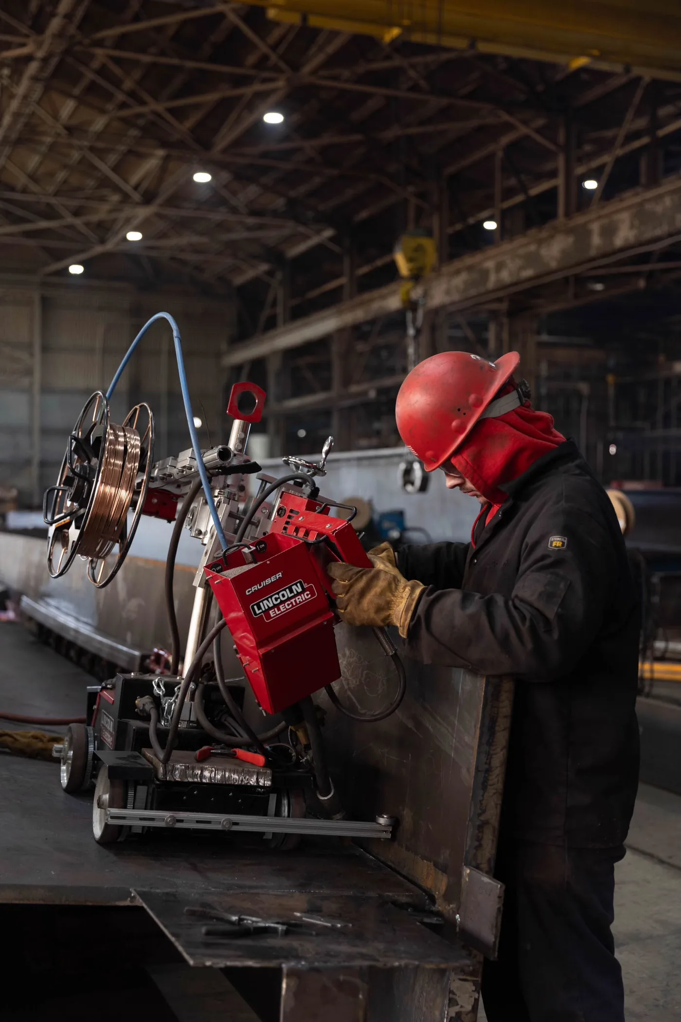 Worker in a red hard hat setting up an automated welding carriage on a steel girder