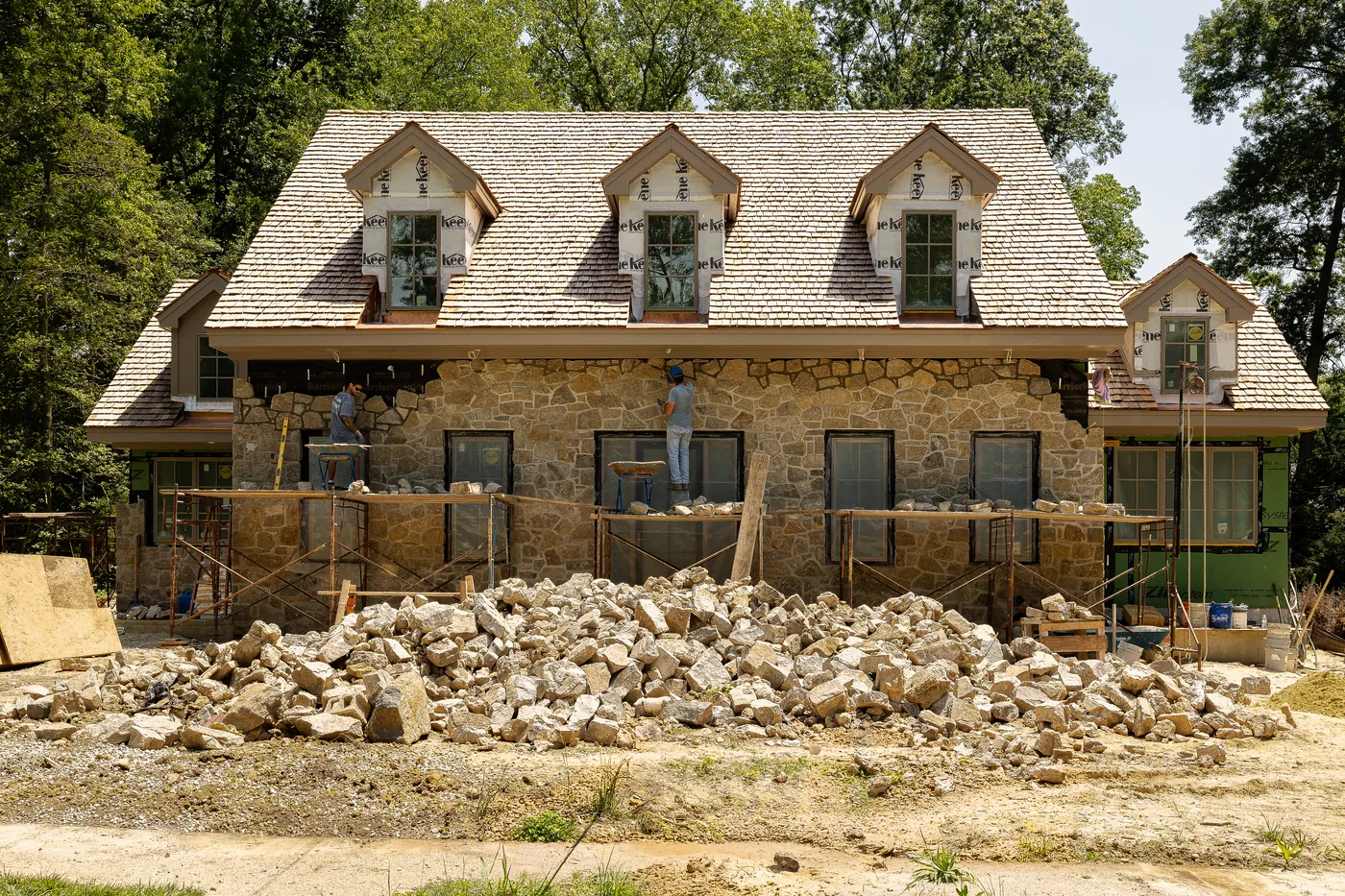 Masons on scaffolding laying a new fieldstone facade, a pile of cut stone in the foreground