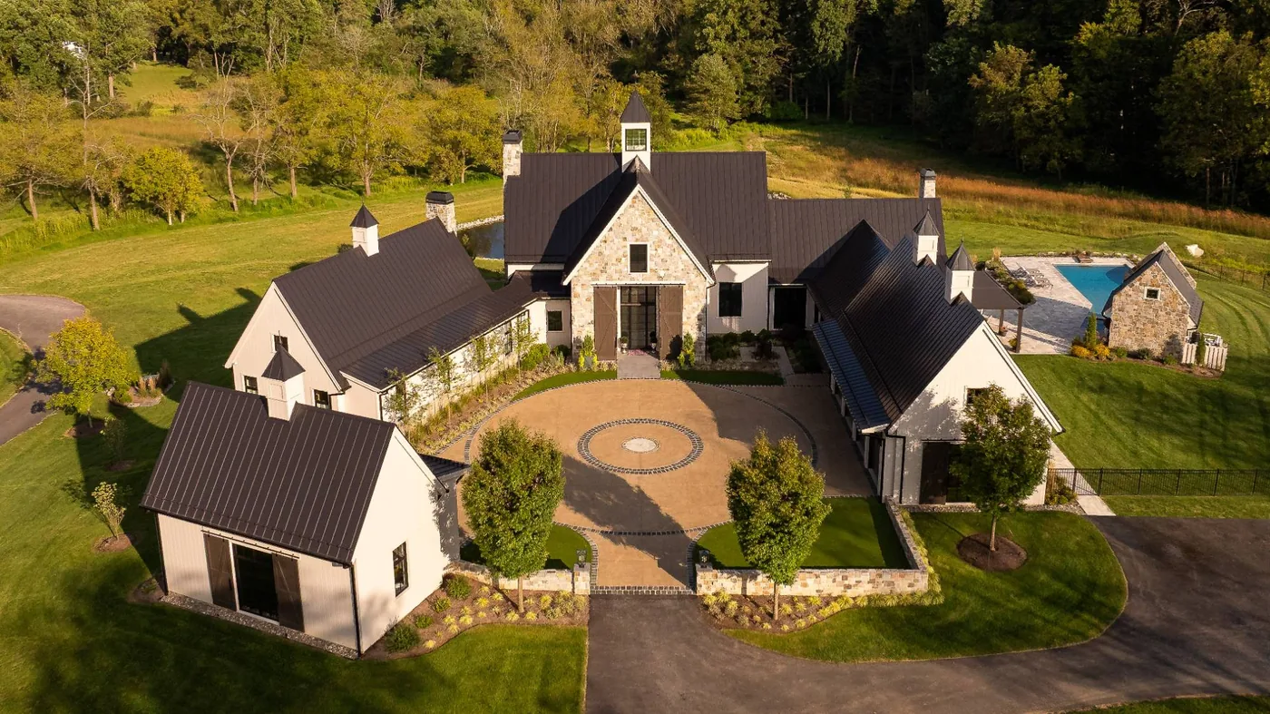 Aerial of a farmhouse estate's motor court with a stone medallion and flanking barns