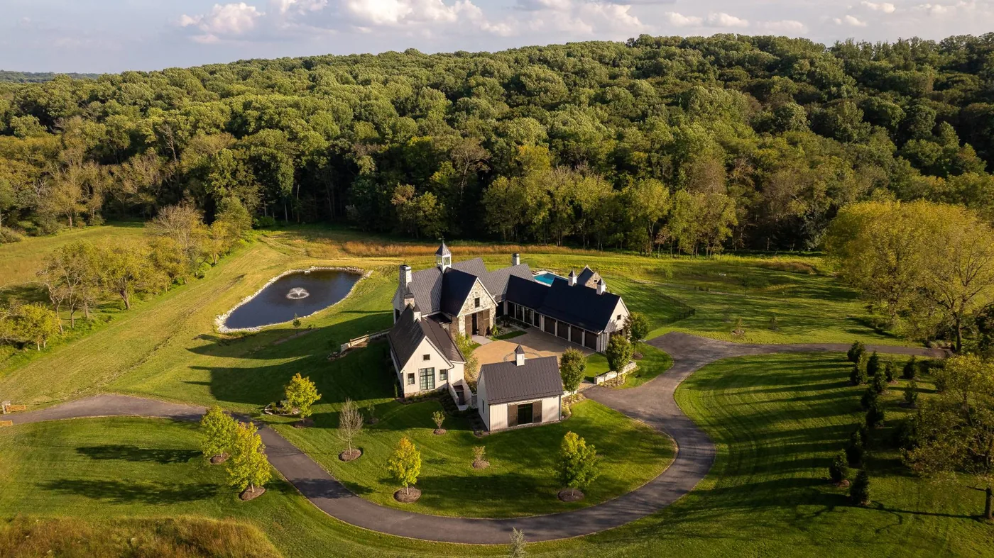 Aerial of a farmhouse estate set among meadows, a pond and forest