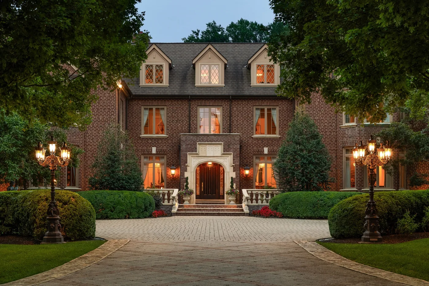 Brick Georgian home at twilight with a lantern lit drive