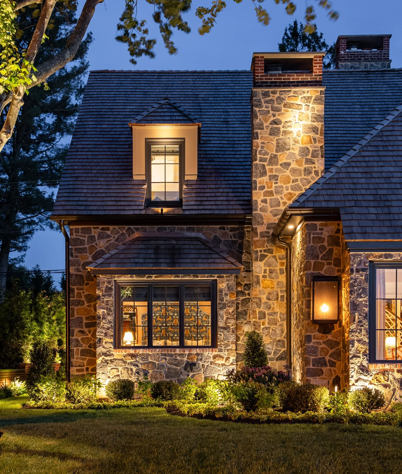 Stone cottage style home at dusk with warm light in every window